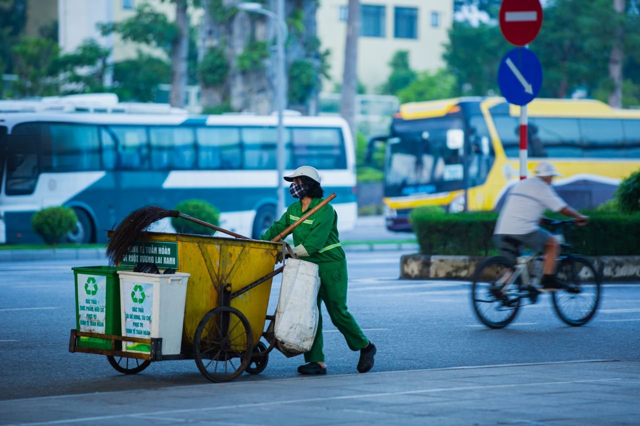 Free Street cleaner pushing cart with recycling bins in a busy urban setting. Stock Photo