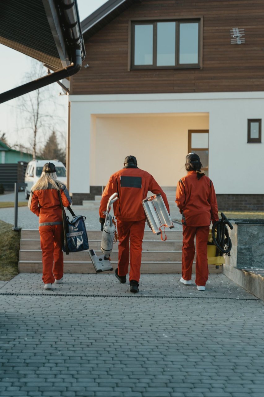 Free Cleaning crew in red uniforms with equipment approaching a modern house exterior. Stock Photo